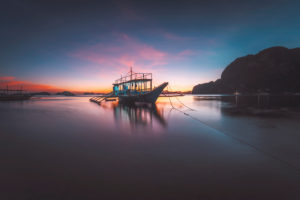 Corong beach, El Nido, Philippines. Soft glow sunset light over horizon on tropical beach with boat in ocean lagoon. Corong beach, El Nido, Philippines. Soft glow sunset light over horizon on tropical beach with boat in ocean lagoon.